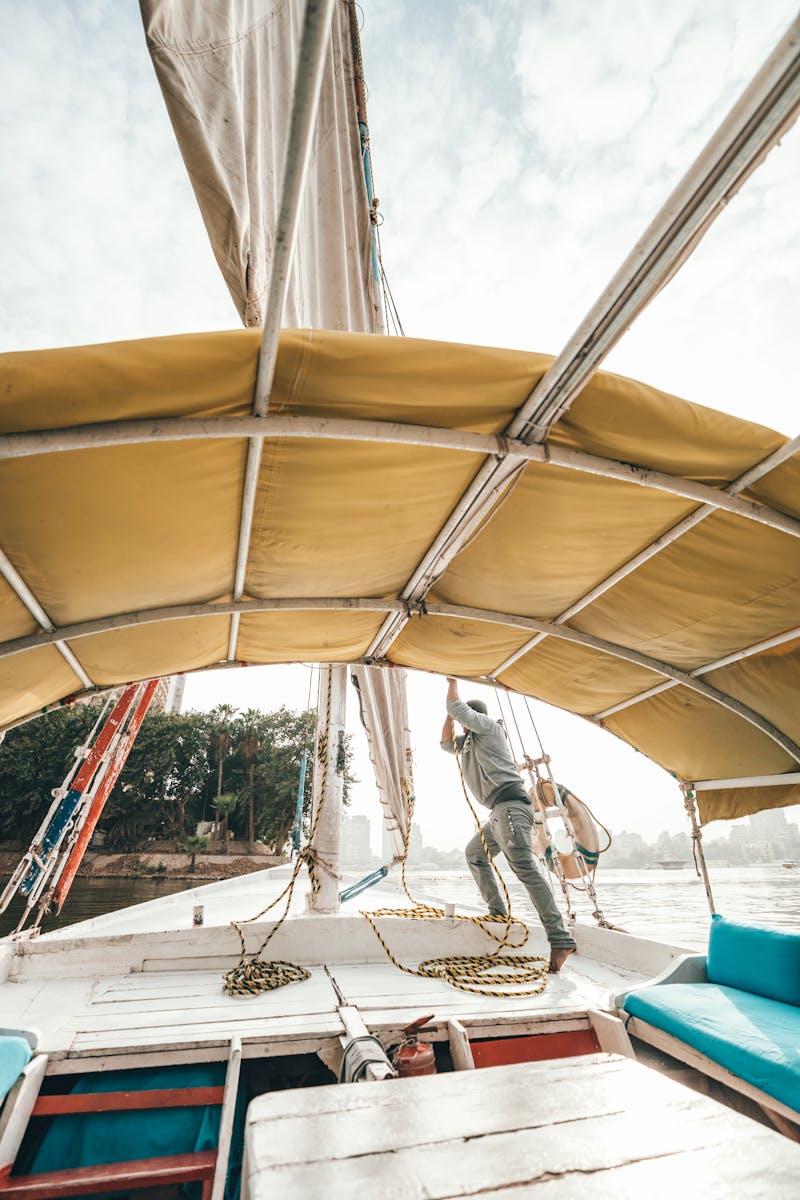 Side view of anonymous male in casual clothes setting sail on traditional boat floating on river on sunny day